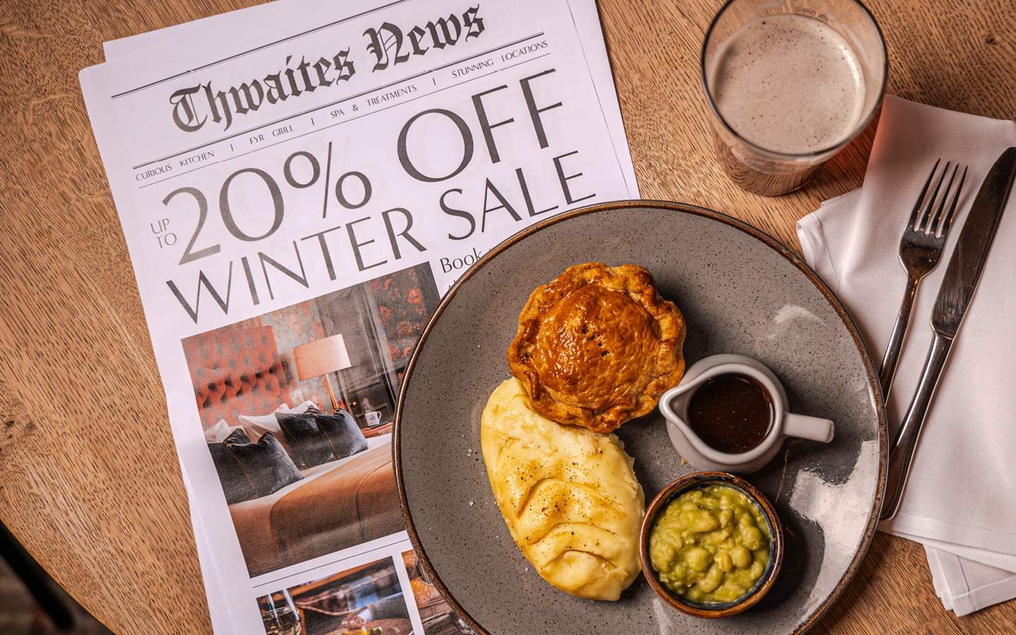 "up to 20% off this winter" newspaper with a pie and a pint flat lay at a pub table